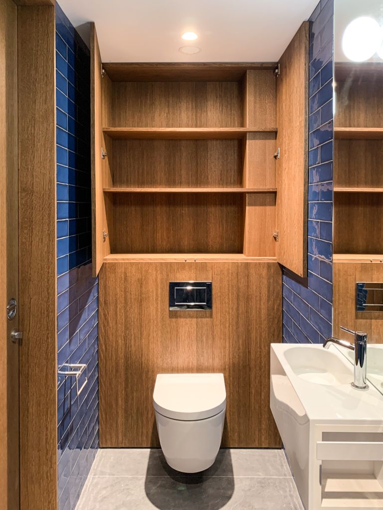 walnut panelled wall behind toilet with matching cupboards above